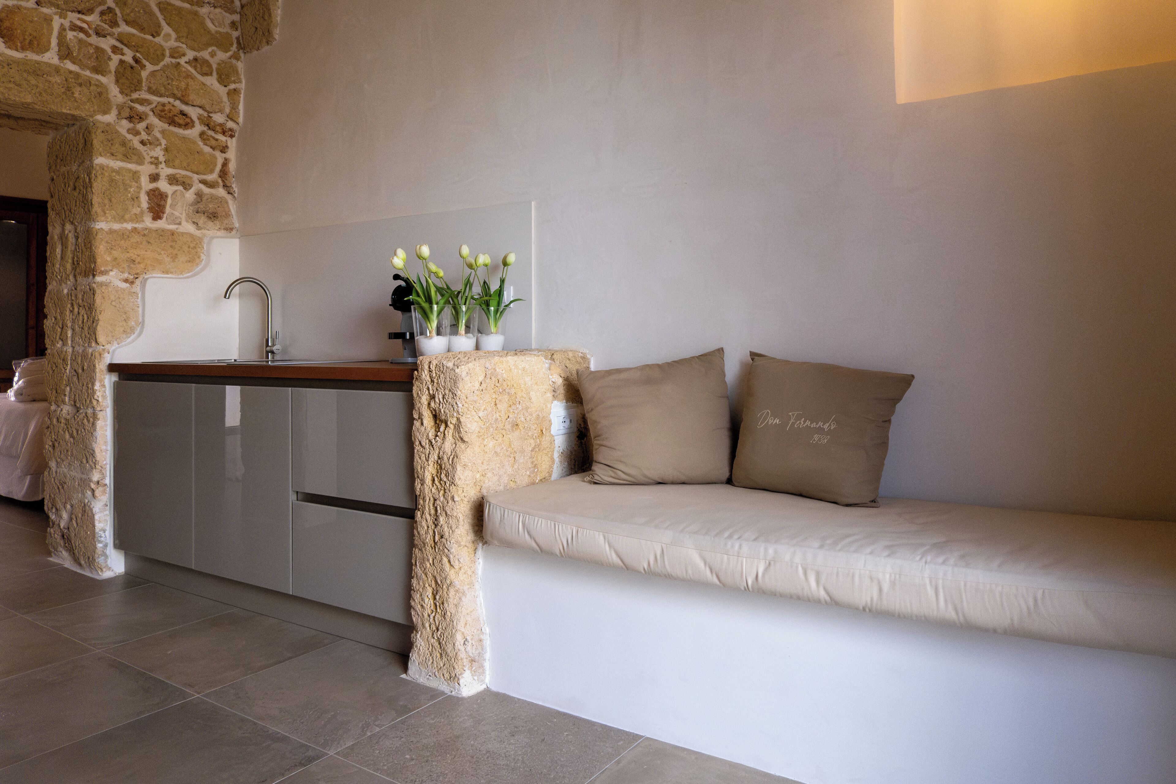 A modern kitchen with a stone accent wall, a built-in bench with cushions, and a small table with potted plants.