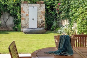 A garden with a stone wall, a water feature, and a wooden table with a blue cloth. - Don Fernando 1938 (Miggiano)