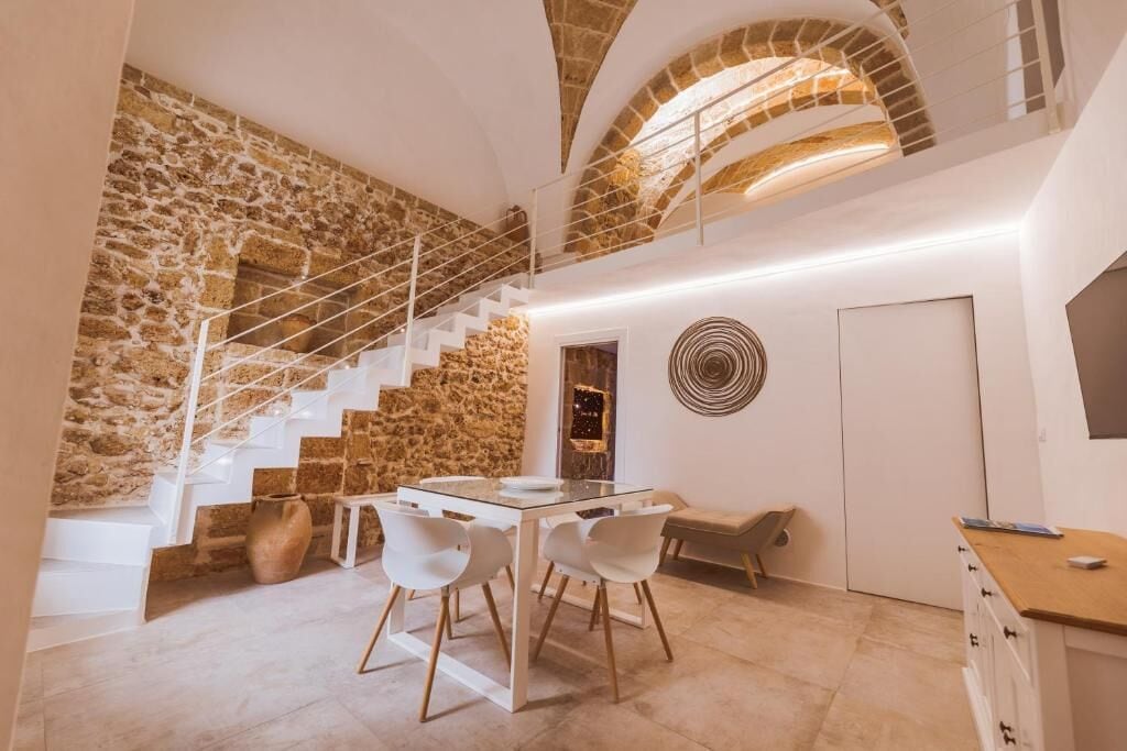 Een modern interieur met een stenen muur, een trap, een eethoek met een glazen tafel en een keuken.