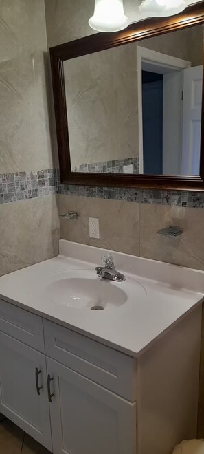 A bathroom with a white sink, a mirror with a wooden frame, and a tiled backsplash. - Sunset At Chalvilles - Peaceful 2-bedroom house with AC in The Valley (East End Village)