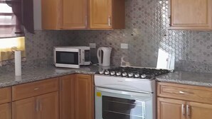 A kitchen with wooden cabinets, a microwave, a kettle, and a stove. - Sunset At Chalvilles - Peaceful 2-bedroom house with AC in The Valley (East End Village)