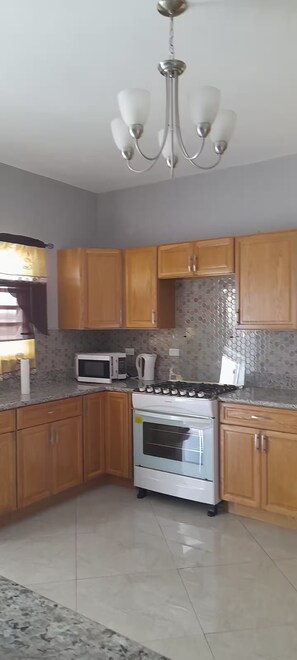 A kitchen with wooden cabinets, a microwave, a kettle, and a stove. - Sunset At Chalvilles - Peaceful 2-bedroom house with AC in The Valley (East End Village)