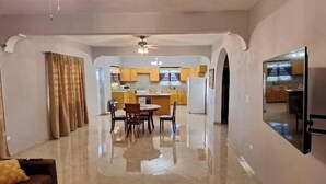 A spacious living area with a dining table and chairs, a sofa, and a kitchen in the background. - Sunset At Chalvilles - Peaceful 2-bedroom house with AC in The Valley (East End Village)