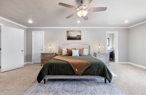 Ein Schlafzimmer mit einem großen Bett, einem Deckenventilator, einem Nachttisch, einer Kommode und einem Gemälde an der Wand.