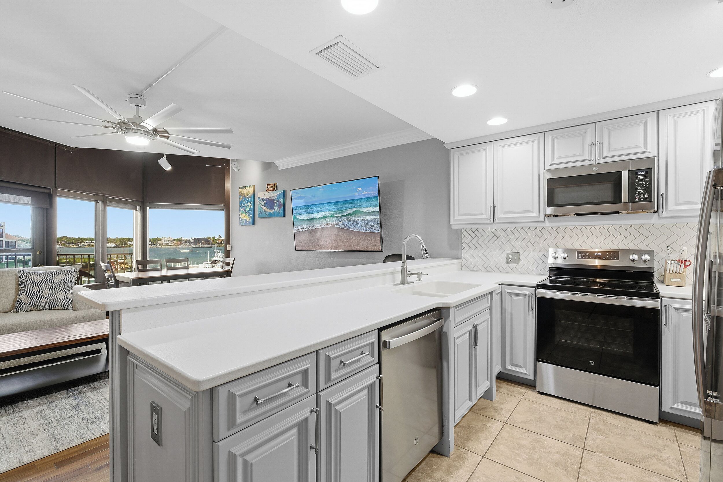 Una cocina moderna con armarios blancos, una isla grande, electrodomésticos de acero inoxidable y vistas al exterior.
