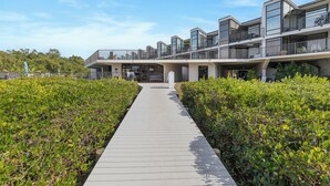 Un edificio moderno con numerosi balconi e una passerella centrale circondata da vegetazione.