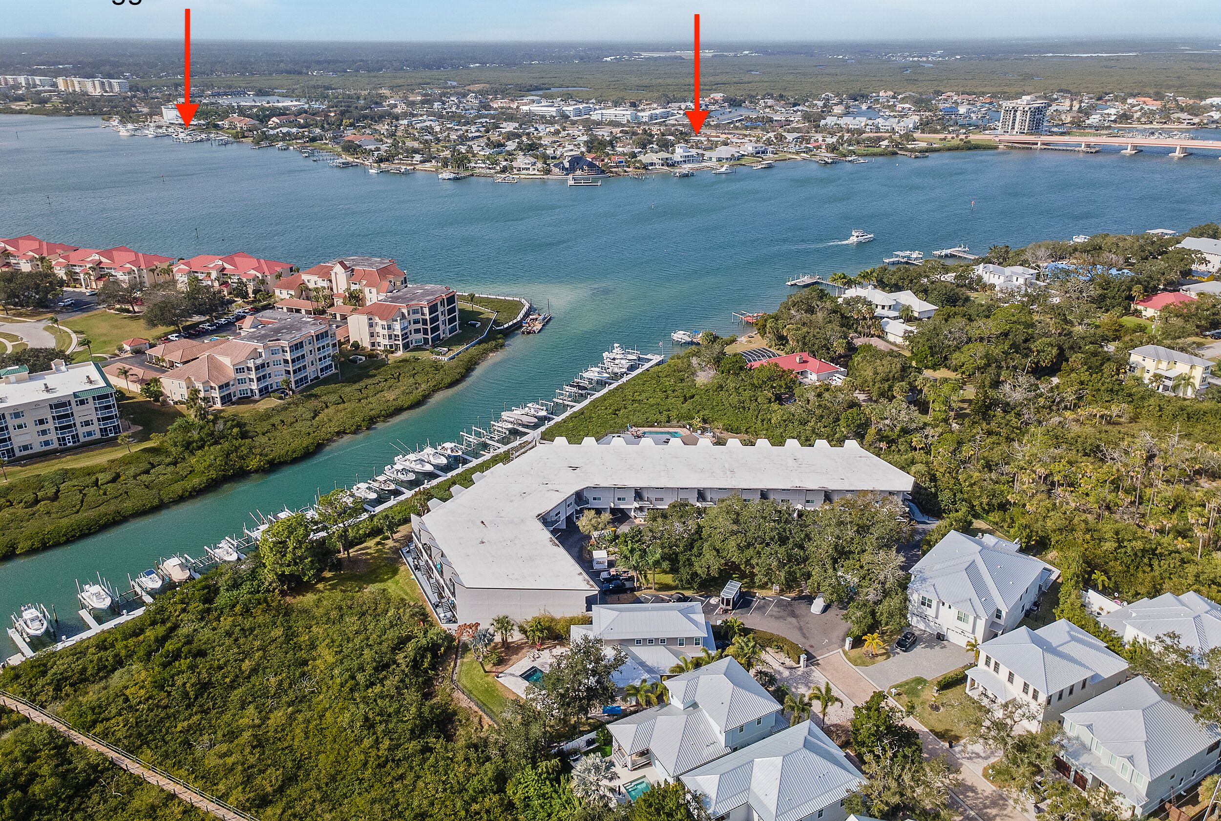 An aerial view of a coastal residential area with a marina, houses, and a large building with a curved roof.