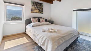 A bedroom with a bed, a window with a view, a painting on the wall, and a wooden ceiling. - Holiday Home 'Quinta do Rio Douro - Rural Tourism' with Mountain View, Pool and AC (Douro)