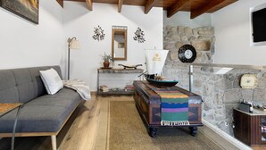 A cozy room with a sofa, a wooden table with a colorful table runner, a stone wall, and a fireplace. - Holiday Home 'Quinta do Rio Douro - Rural Tourism' with Mountain View, Pool and AC (Douro)