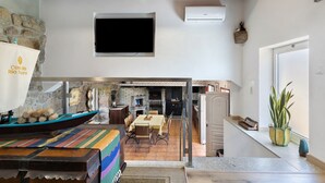 A dining area with a table and chairs, a stone wall, and a television mounted on the wall. - Holiday Home 'Quinta do Rio Douro - Rural Tourism' with Mountain View, Pool and AC (Douro)