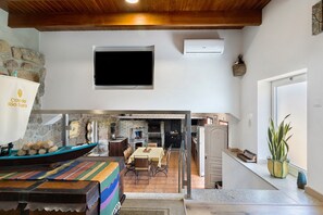 A dining area with a table and chairs, a stone wall, and a television mounted on the wall. - Holiday Home 'Quinta do Rio Douro - Rural Tourism' with Mountain View, Pool and AC (Douro)