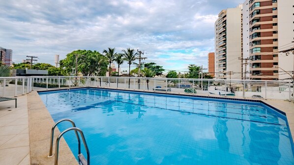 A rectangular swimming pool with a metal ladder on the left, surrounded by a white fence. - Apto com 3 su tes Piscina e Sauna a 450m da Praia (Salvador)