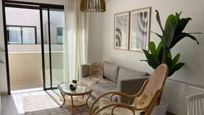 Ein modernes Wohnzimmer mit einer Couch, zwei Korbstühlen, einem Glastisch und einer großen Topfpflanze.