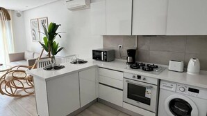 Eine moderne Küche mit weißen Schränken, einem Backofen, einer Mikrowelle, einer Kaffeemaschine und einer Waschmaschine.