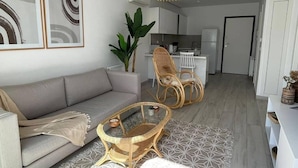 Ein modernes Wohnzimmer mit einem grauen Sofa, Korbstühlen, einem Glastisch und einem Teppich mit geometrischem Muster.