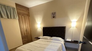 A hotel room with a bed, two bedside tables, a wall-mounted light, a wooden wardrobe, and a door. - Relaxation and comfort in a private apartment (Roldanillo)