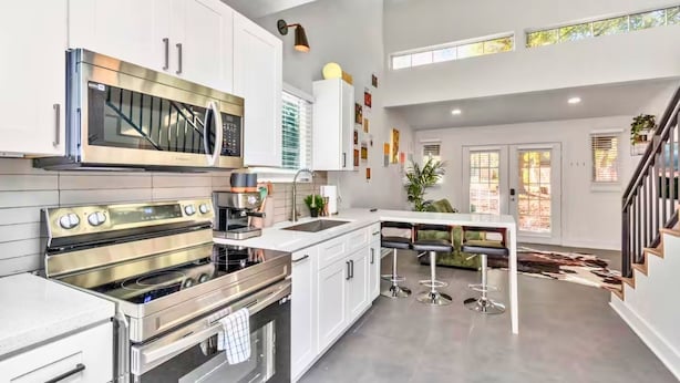 A modern kitchen with stainless steel appliances, white cabinetry, and a bar area with stools. - Loft Jason | Relaxing Lake Conroe Getaway (Montgomery)