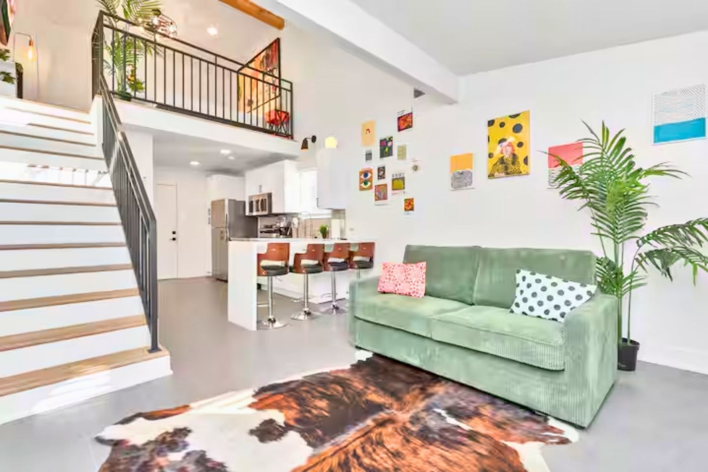 Una sala de estar moderna con un sofá verde, un tapete de cuero de vaca y una escalera que sube a un nivel superior.