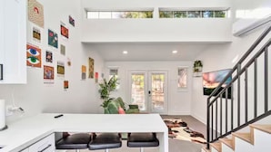 A modern kitchen with a white countertop, a bar stool area, and a staircase leading to an upper level. - Loft Jason | Relaxing Lake Conroe Getaway (Montgomery)