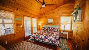 A wooden cabin bedroom with a bed, two bedside tables, a ceiling fan, and a window with blinds. - Anisidi | New River Waterfront • Pet Friendly (Pulaski County)