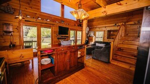 A wooden cabin interior with a kitchen, dining area, and a staircase. - Anisidi | New River Waterfront • Pet Friendly (Pulaski County)