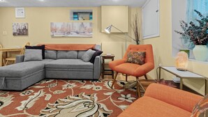 En stue med en grå hjørnesofa, en orange lænestol, et lille bord og en gulvlampe.