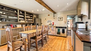Un'ampia cucina con pavimento in legno, un'isola centrale con piano cottura ed elementi a scaffale contenenti stoviglie.