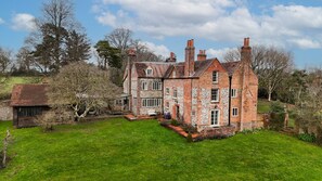 A large, historic brick house with multiple chimneys, surrounded by a well-maintained lawn and trees. - Huckleberry Farm House (Goring)