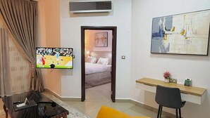 Ein modernes Wohnzimmer mit einer Couch, einem Couchtisch, einem Fernseher, einem Schreibtisch und einem Bild an der Wand.