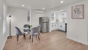 Une cuisine moderne avec des meubles blancs, un réfrigérateur en acier inoxydable et un coin repas comprenant une table en verre et des chaises grises.