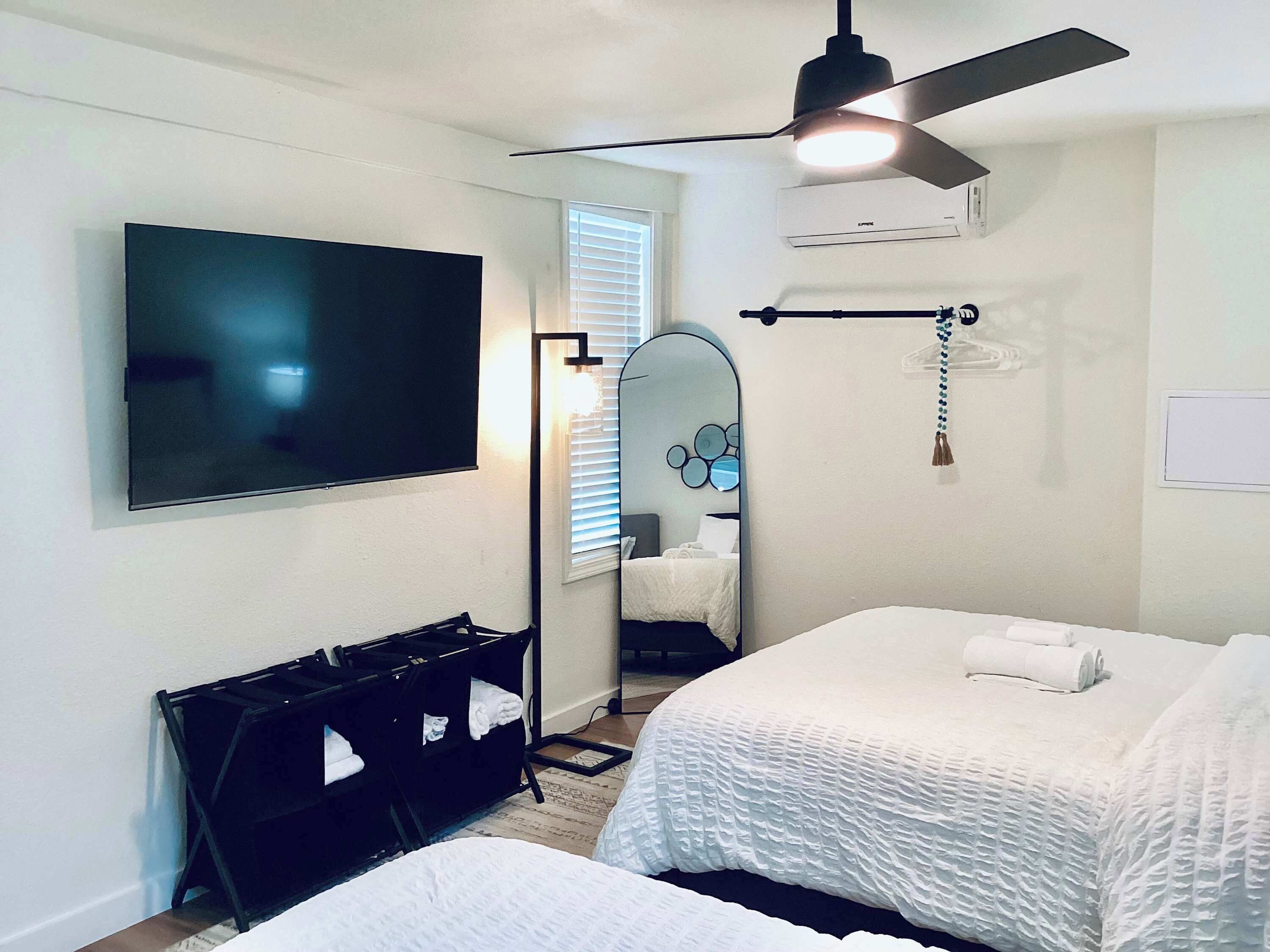 A hotel room with two beds, a ceiling fan, a TV, a mirror, and a black storage unit.