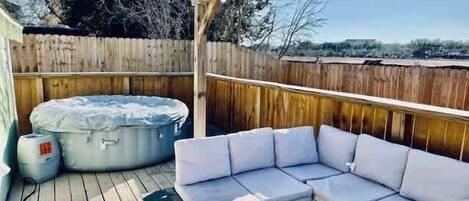 A covered outdoor patio with a hot tub, a white sectional sofa, and a small table.