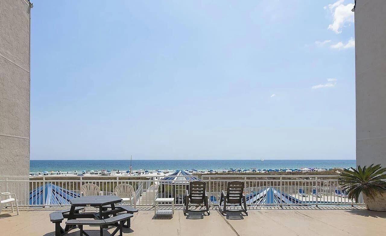 A balcony with a view of the beach, outdoor seating, and a palm tree.