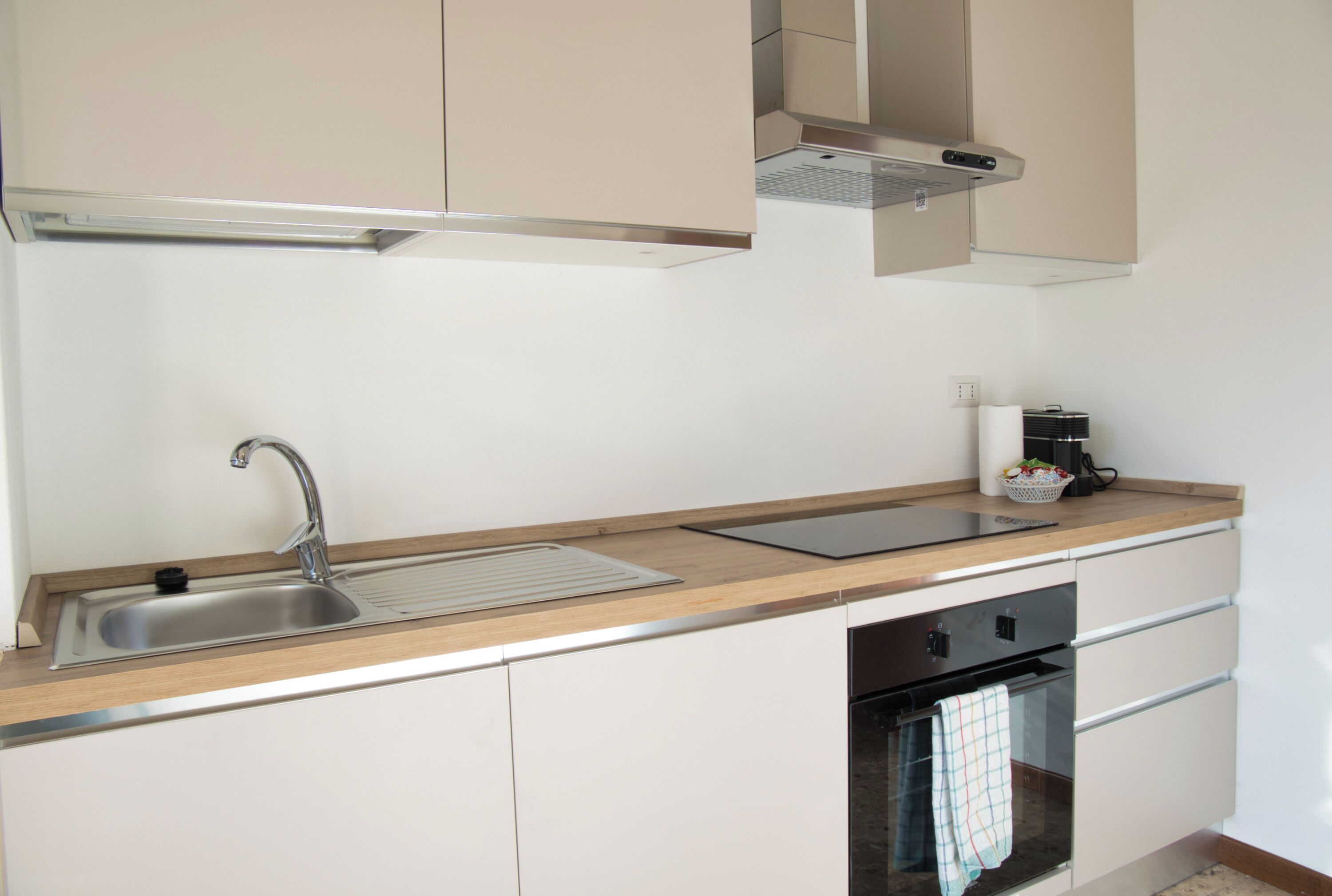 A modern kitchen with a stainless steel sink, wooden countertop, built-in oven, and white cabinets.