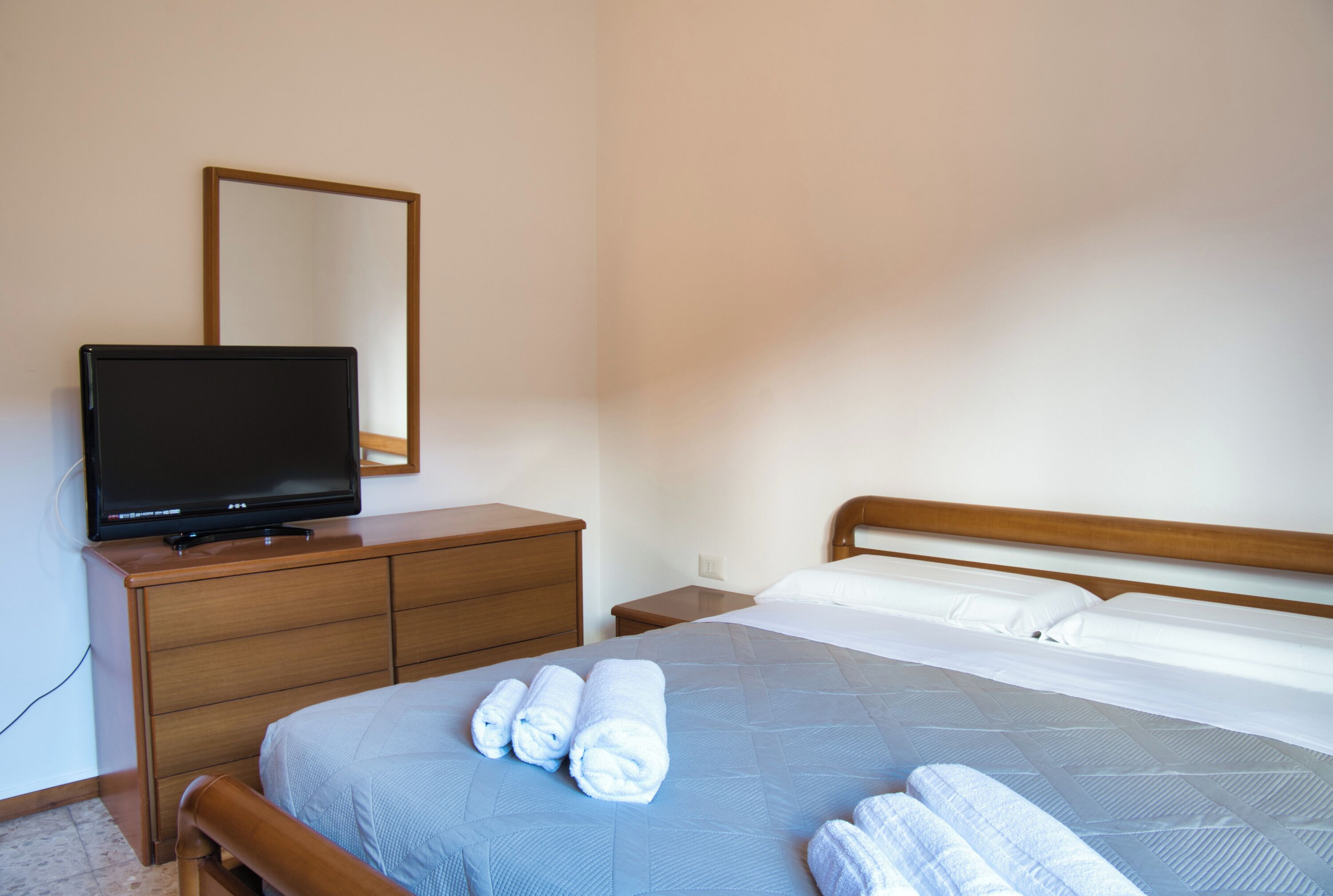 A hotel room with a bed, a wooden dresser, a television, and a mirror.