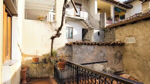 Un patio estrecho con baldosas de terracota, una cerca de hierro forjado y plantas en macetas.