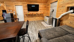 Un intérieur en bois comprenant un téléviseur, un canapé, une table à manger, des chaises et un petit coin cuisine.