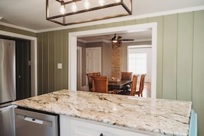 A kitchen with a granite countertop, wooden dining table, and chairs, with a brick column and ceiling fan.