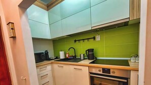 Uma cozinha compacta com armários brancos, painel de parede verde, forno embutido e uma pia.