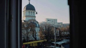 Vista de um edifício com cúpula e um campanário, uma rua com carros estacionados e um prédio amarelo com um letreiro.