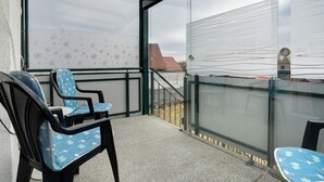 Ein Balkon mit Stühlen, einer Glastür und Blick auf ein Gebäude mit einer gemusterten Wand.