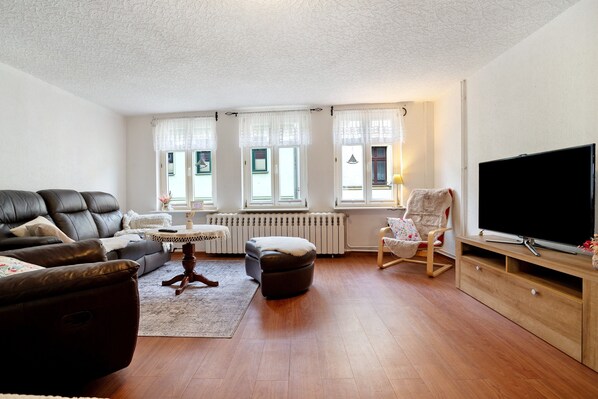 A living room with a sofa, ottoman, TV stand, and a chair.