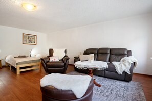 A furnished living room with a bed, a leather armchair, a sofa, and a small table with a lace tablecloth.