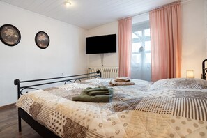 A bedroom with a bed, a flat-screen TV, a window with curtains, and a radiator.