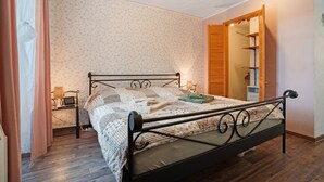 Ein Schlafzimmer mit einem Metallbettgestell, einem Nachttisch mit Lampe, einem Kleiderschrank und einer Wand mit floralem Muster.
