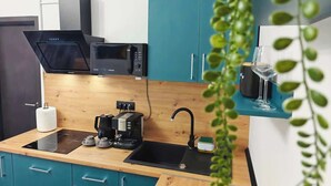 Eine kompakte Küche mit türkisfarbenen Schränken, einer schwarzen Mikrowelle, einer Kaffeemaschine und einem Spülbecken.