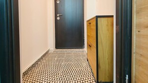 Ein schmaler Flur mit einem gemusterten Boden, einer dunklen Tür und einem Holzschrank.