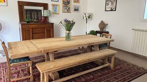 Un coin repas avec une table et des bancs en bois, entouré d’un tapis à motifs, avec un miroir au-dessus de la table et divers tableaux encadrés accrochés aux murs.