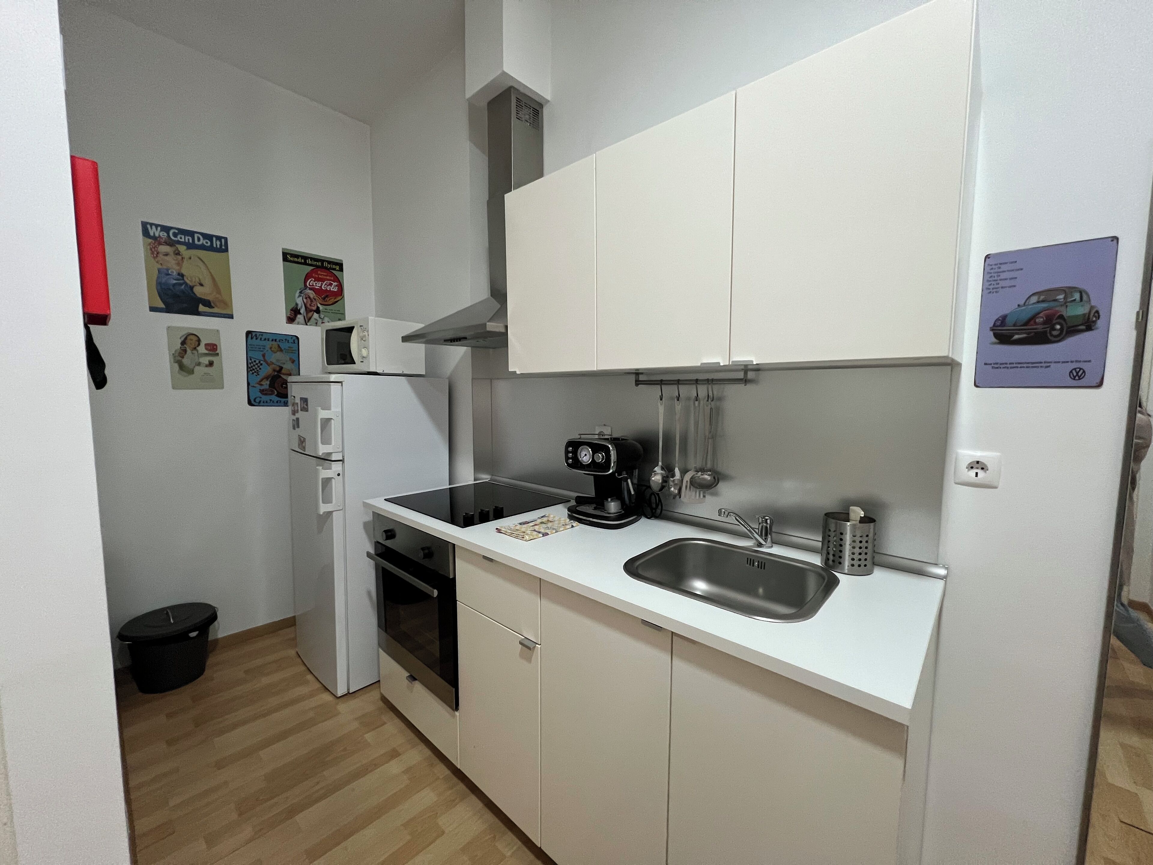 A compact kitchen with white cabinets, a microwave, a coffee maker, and a sink.
