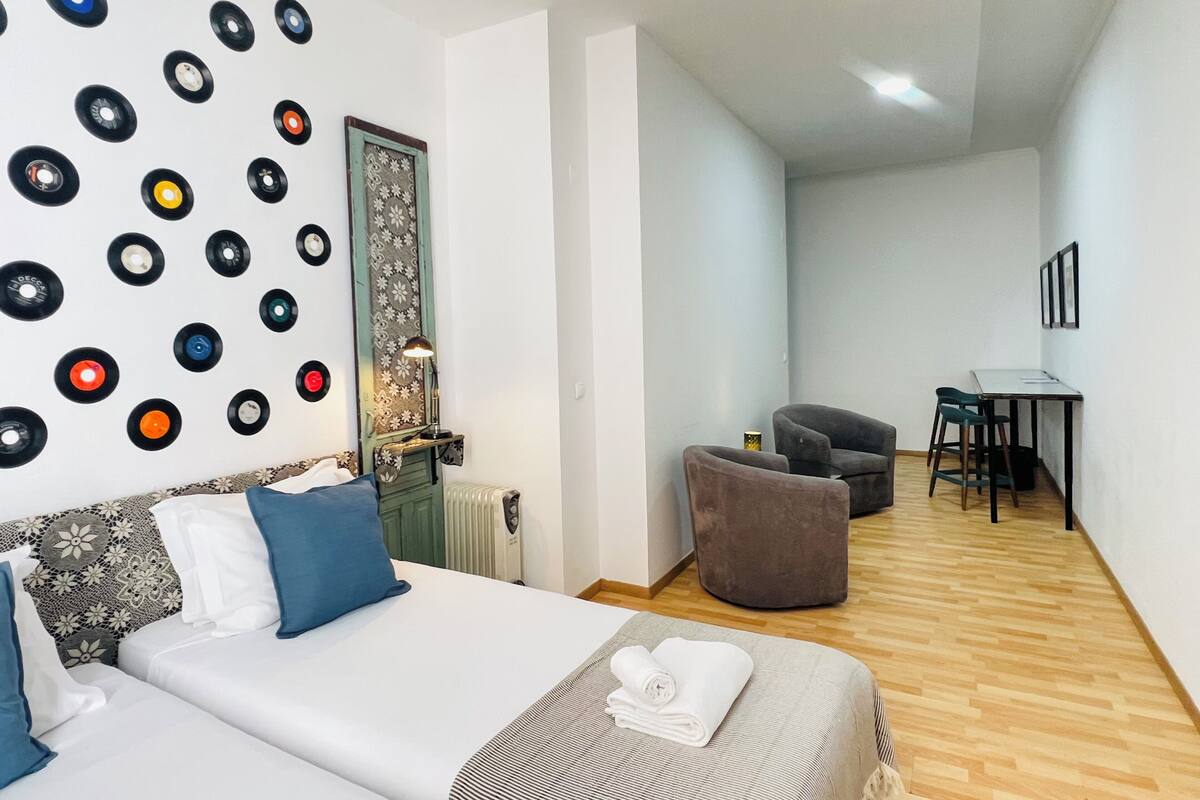 Une chambre d’hôtel équipée d’un lit, d’un bureau, d’une chaise et dont le mur est décoré de disques vinyle.